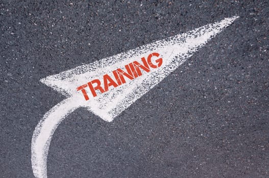 Directional white painted arrow with word TRAINING over road surface, concept image