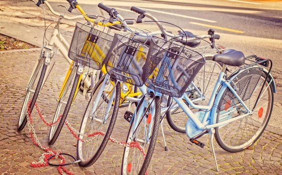 Four parked bicycles on the sidewalk, chained together. Vintage style
