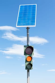 Road traffic light powered by electricity generated from a solar panel. Blue sky