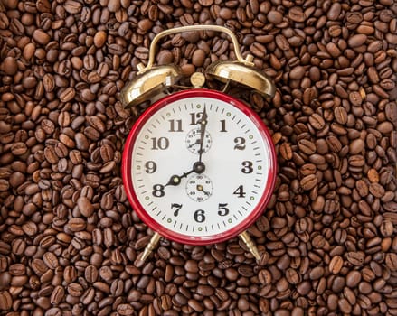 Vintage alarm clock shows 8 o'clock on background of coffee beans