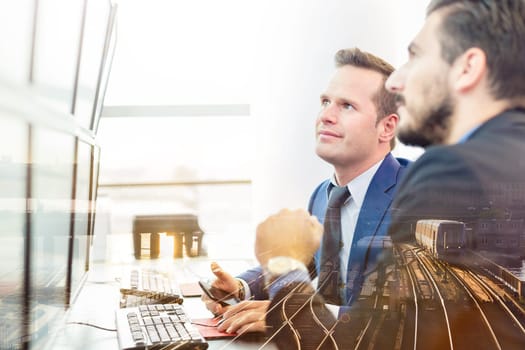 Successful businessmen trading stocks. Equity traders looking at on multiple computer screens in conteporary office. City reflection in window. Business success concept.