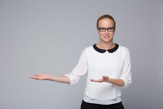 Beautiful young businesswoman smiling, holding open palm with empty copy space. Business woman showing hand sign to side, concept of advertisement product. Grey background.