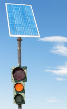 Road traffic light powered by electricity generated from a solar panel. Blue sky