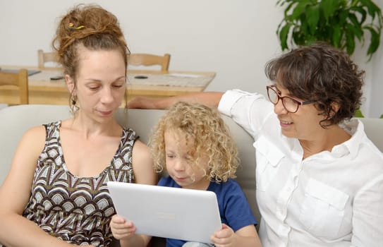 a child and his mother and his grandmother play with tablet