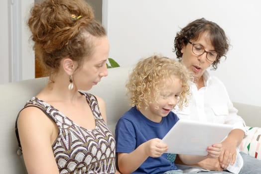a child and his mother and his grandmother play with tablet