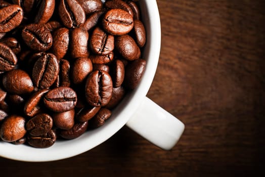 Fresh coffee beans in cup on wooden background