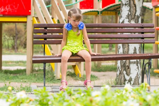 Crying girl sitting on the bench on the background of the playground