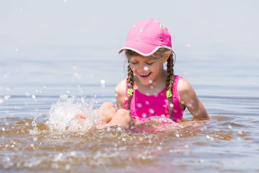 Girl splashing in cap sitting on a shelf in water