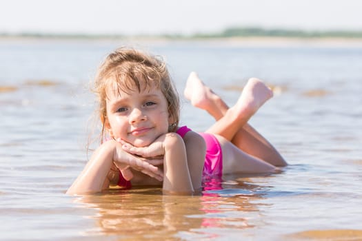 Five-year girl lies in water in the shallows of the river