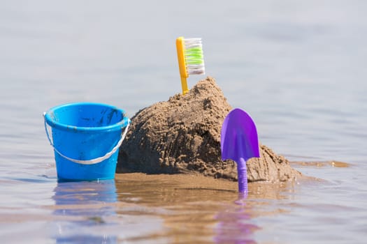 Construction of a sand castle, next to which stands a shovel and bucket on the shallows of the river