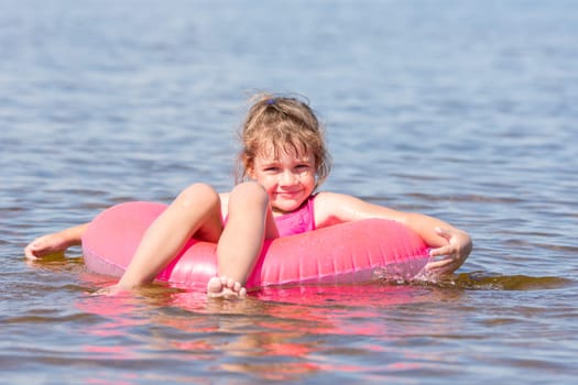 Five-year girl swims in the river sat on the lap swimming and happily looks into the frame