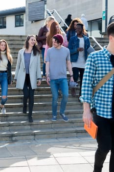 A group of young teenage students smile as they walk through the city on a break from university. They are carrying their books and digital tablets.