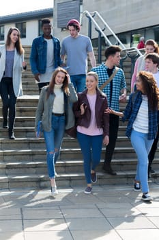 A group of young teenage students smile as they walk through the city on a break from university. They are carrying their books and digital tablets.
