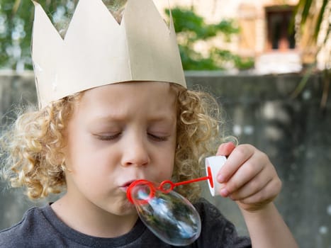 a little blond boy makes bubbles in the garden