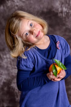 little girl with mandarin orange in front of brown background