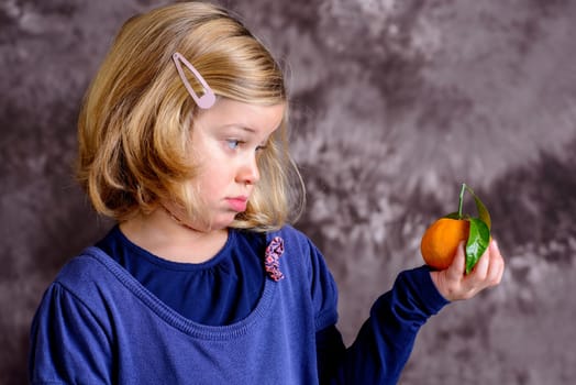 little girl with mandarin orange in front of brown background