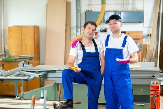 two worker in blue dungarees in a carpenter's workshop