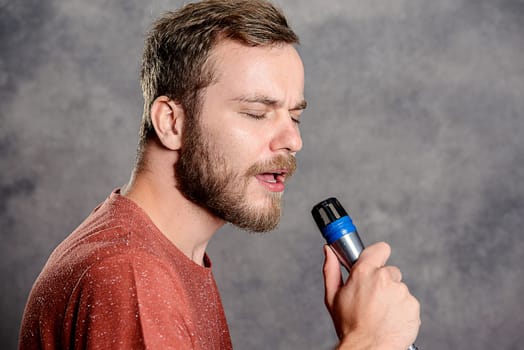 young bearded man in red shirt singing in microphone