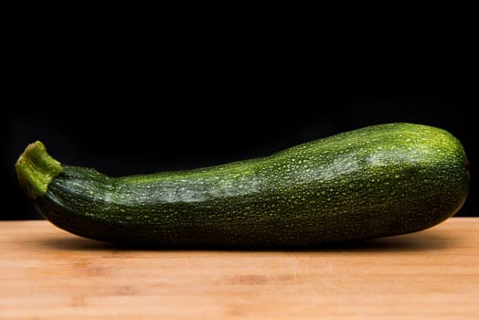  close up on zucchini courgette on wood and black background