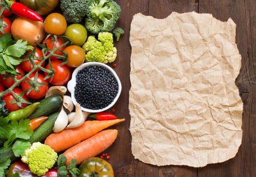 Uncooked black lentils in a bowl with vegetables on a wooden table