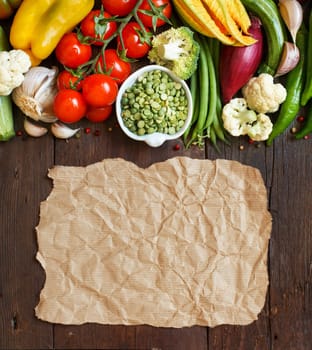 Green peas in a bowl with fresh vegetables with craft paper on wood top view