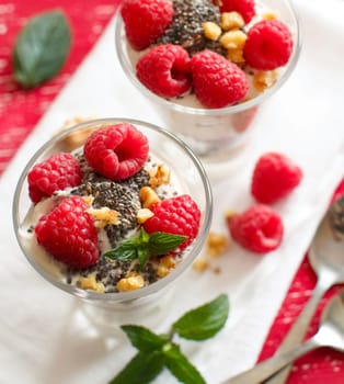 Yogurt with chia seeds, walnuts, mint and raspberries on red background