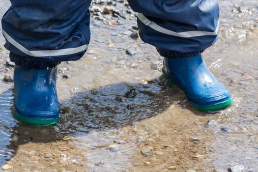 Child with blue rubber boots in a puddle. Close-up..