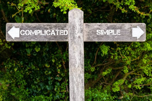 Wooden signpost with two opposite arrows over green leaves background. SIMPLE versus COMPLICATED directional signs, Choice concept image