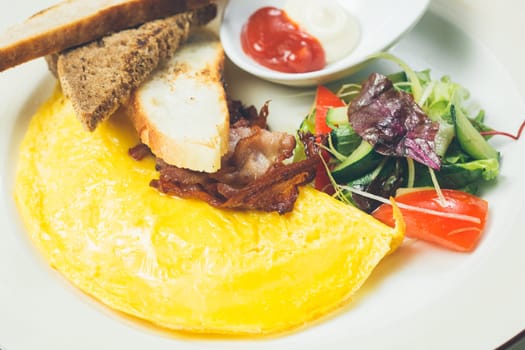 Omelet with bacon served on white plate, vegetables aside. Warm colors. Shallow dof.