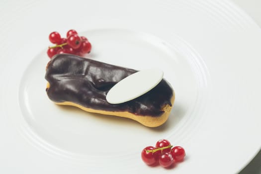 Single chocolate eclair with space for text on white  plate. Warm colors. Shallow dof.
