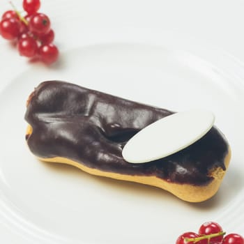Single chocolate eclair with space for text on white  plate. Warm colors. Shallow dof.