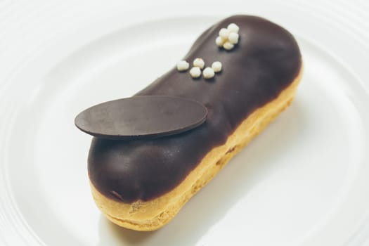 Single chocolate eclair with space for text on white  plate. Warm colors. Shallow dof.