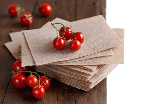 Raw lasagna sheets and cherry tomatoes on a wooden table