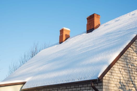 Two brick chimneys on a brick house with a snow covered roof