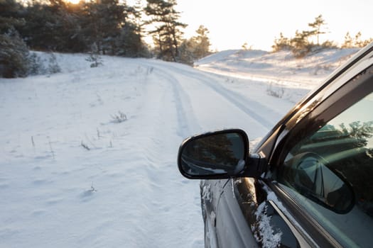 A black cars left mirror during winter on a snowy road
