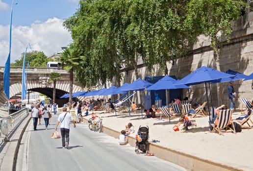 people lying in the sun on the banks of the seine in paris