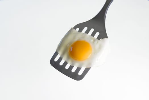 Fried egg on the spatula, ready to be served. White background.
