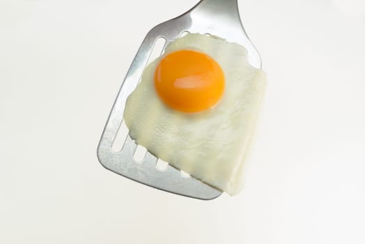 Fried egg on the spatula, ready to be served. White background.