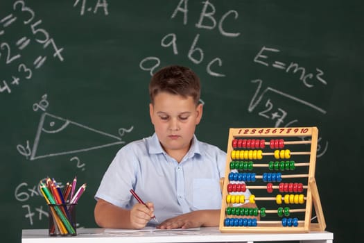 Young boy described at the green blackboard at school thinking about the task