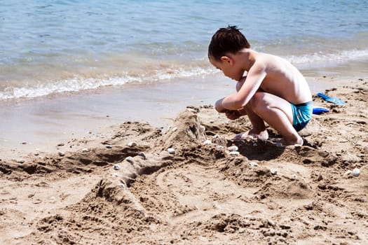 little boy in blue sea playing with mud pies and sand