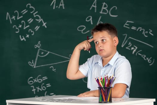 Young boy described at the green blackboard at school thinking about the task