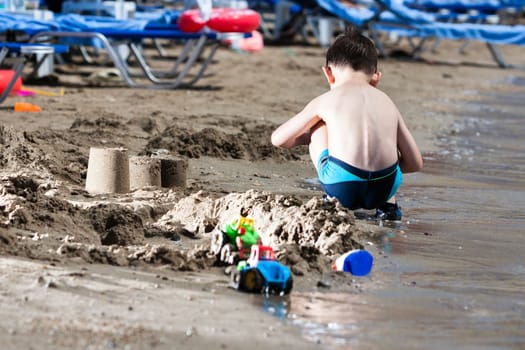 little boy in blue sea playing with mud pies and sand