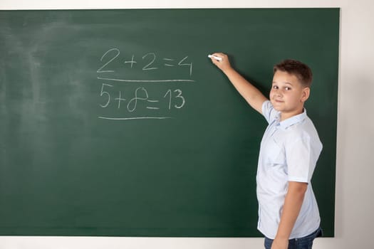 Young boy writing mathematical examples on the a school blackboard