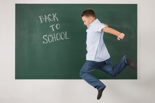 Young boy jumping in a green chalkboard with the words back to school
