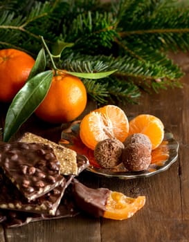 Chocolate, truffles and tangerins with fir on a wooden table