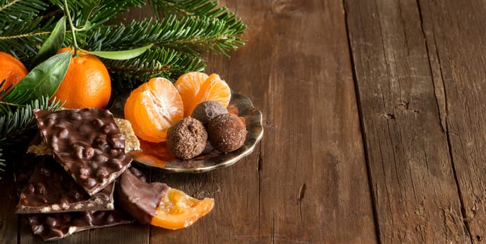 Chocolate, truffles and tangerins with fir on a wooden table