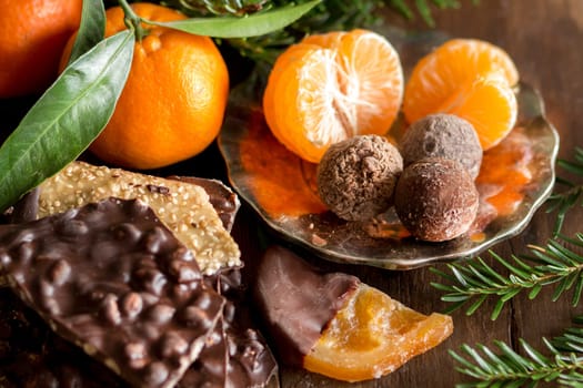 Chocolate, truffles and tangerins with fir on a wooden table