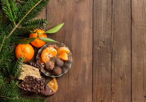 Chocolate, truffles and tangerins with fir on a wooden table