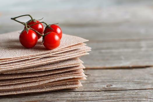 Raw lasagna sheets and cherry tomatoes on a wooden table close up