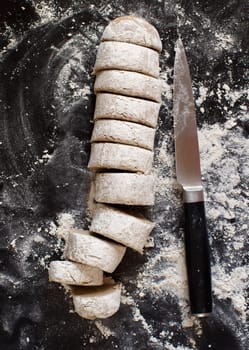 Pieces of raw dough with a knife on a dark background
